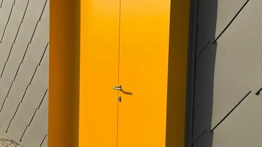 detailní záběr na sytě žluté vstupní dveře do objektu opláštěného odolnými PREFA falcovanými šablonami 44 x 44 v elegantní šedé barvě