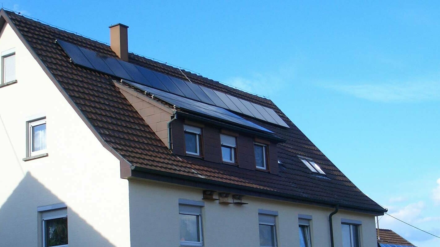 Rodinný dům se střechou z pálených tašek, která potřebuje sanaci; na střeše je vikýř a fotovoltaický systém.