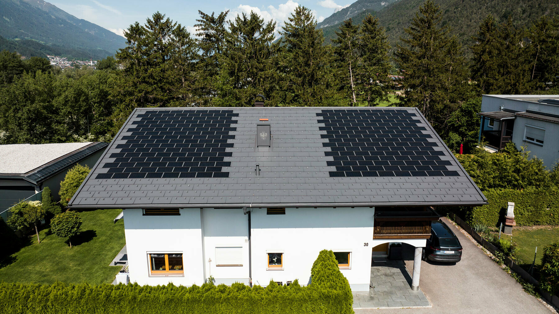 Rodinný dům pokrytý malým integrovaným solárním panelem SDP se střešním panelem R.16 v barvě P.10 tmavě šedé v idylickém prostředí venkova.