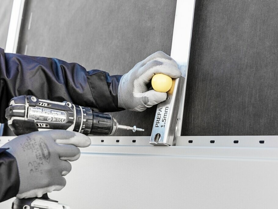 Detailní záběr na klempíře, který instaluje fasádní panel.