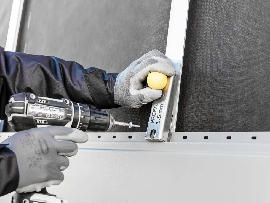 Detailní záběr na klempíře, který instaluje fasádní panel.