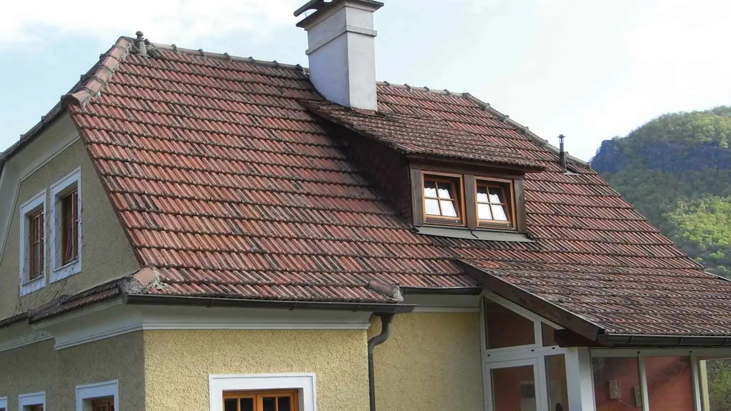 Starý rodinný dům s hrubou žlutou omítkovou fasádou před sanací střechy z pálených tašek