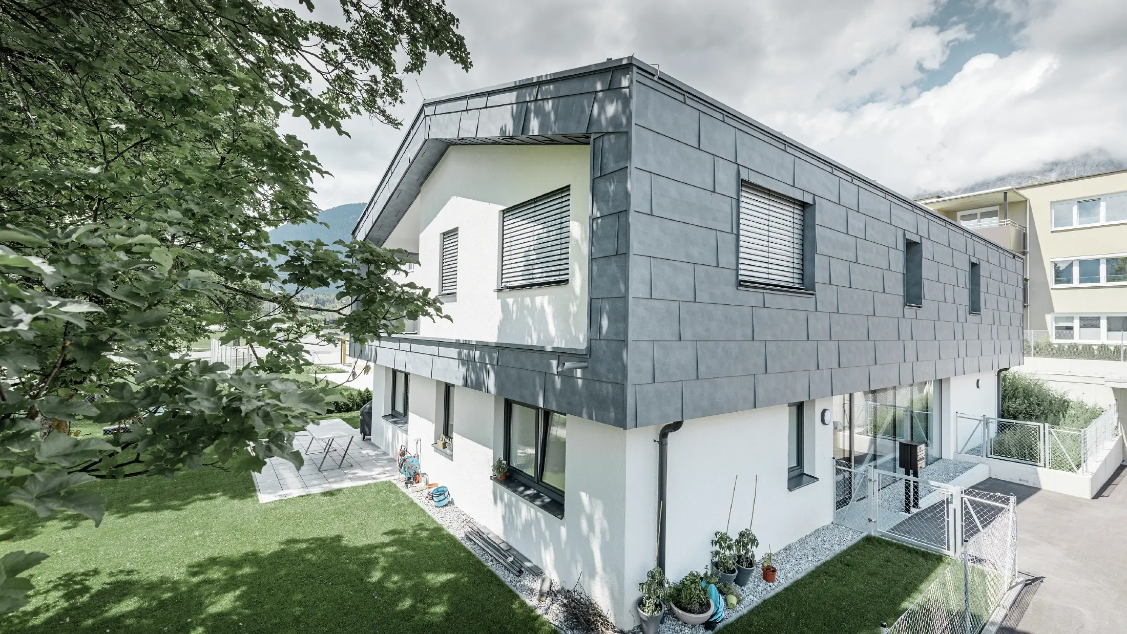 Moderní nástavba obytného domu s plochou sedlovou střechou bez přesahu; fasádní obklad byl proveden pomocí fasádních panelů PREFA FX.12 v barvě břidlicová.