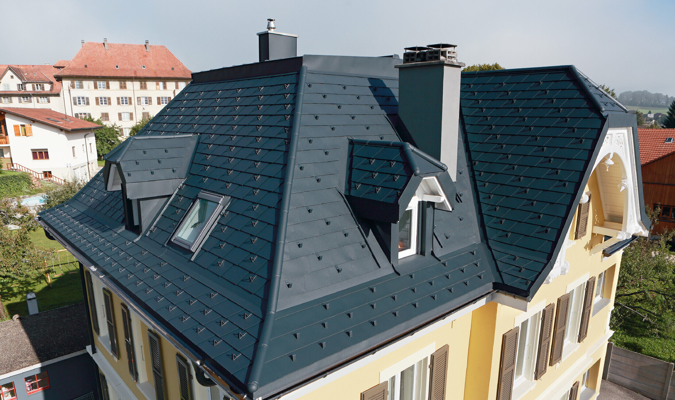 Vila ve Švýcarsku, s mnoha úžlabími a malými vikýři ve střeše; střecha je pokrytá hliníkovým PREFA falcovaným šindelem v barvě P.10 antracitové