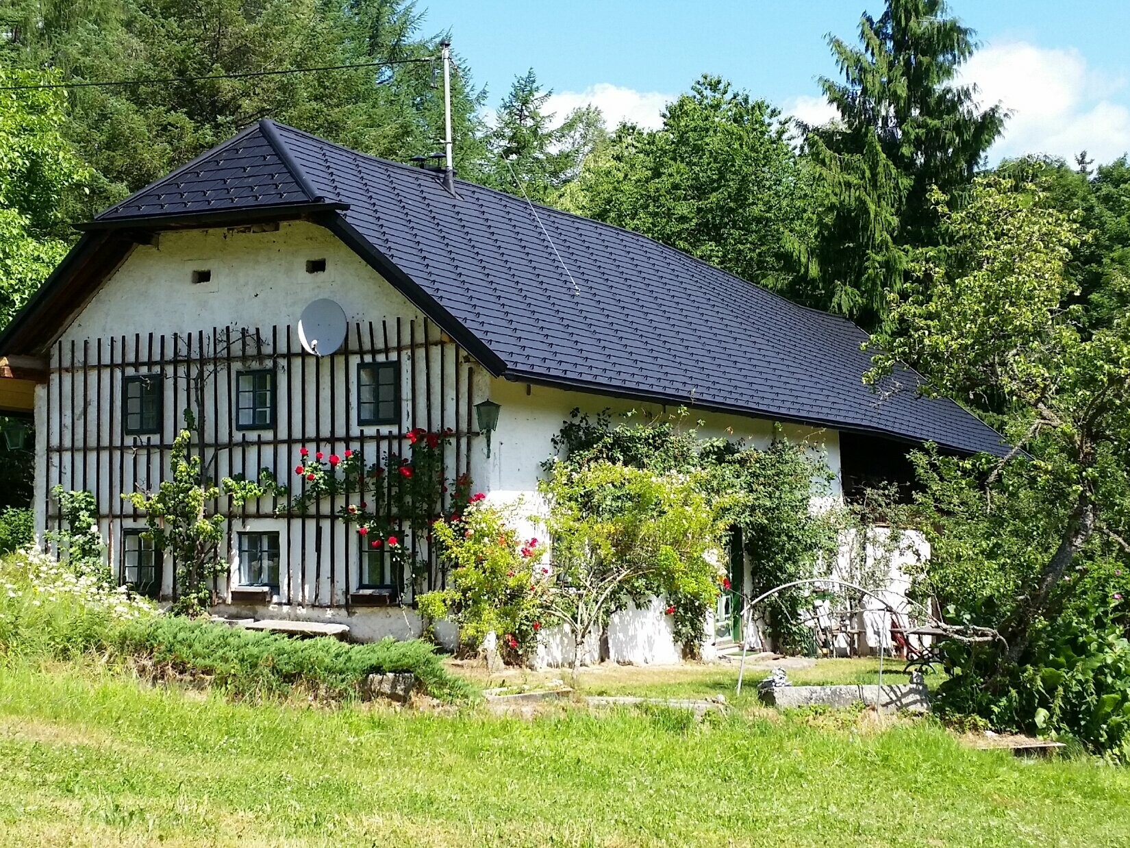 V popředí fotografie je zachycen muž v bílém tričku, který něco vysvětluje. V pozadí je vidět „luční dům“. 400 let stará budova, jejíž střecha byla při rekonstrukci pokryta střešními šindeli PREFA v barvě P.10. 