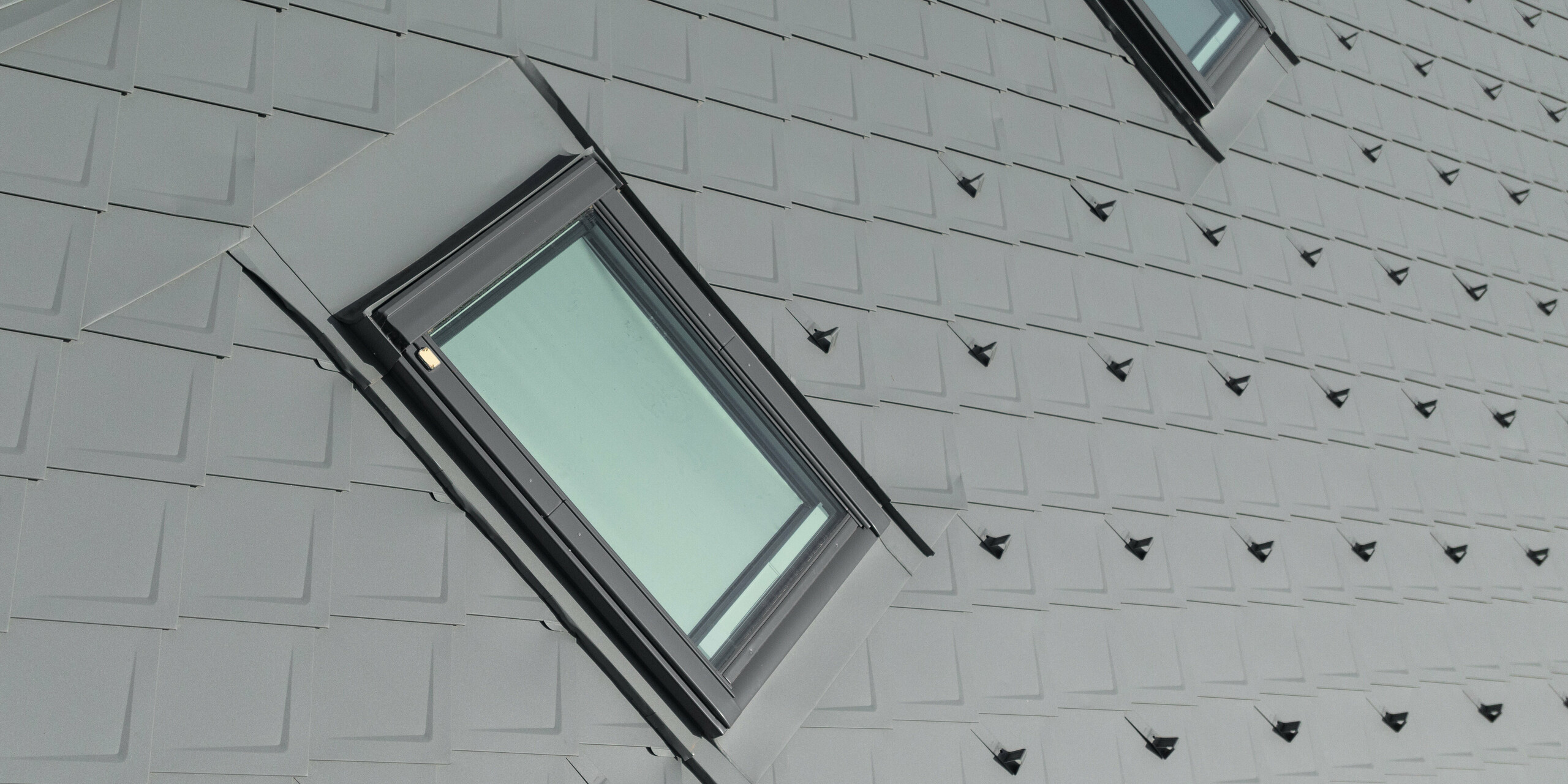 Detail lemování okna z PREFALZ. Lemování nenápadně přechází na pravidelné řady falcovaných šablon 29 x 29 vybavených protisněhovými prvky ve formě sněhových háků. Vše v barvě P. 10 světle šedé.