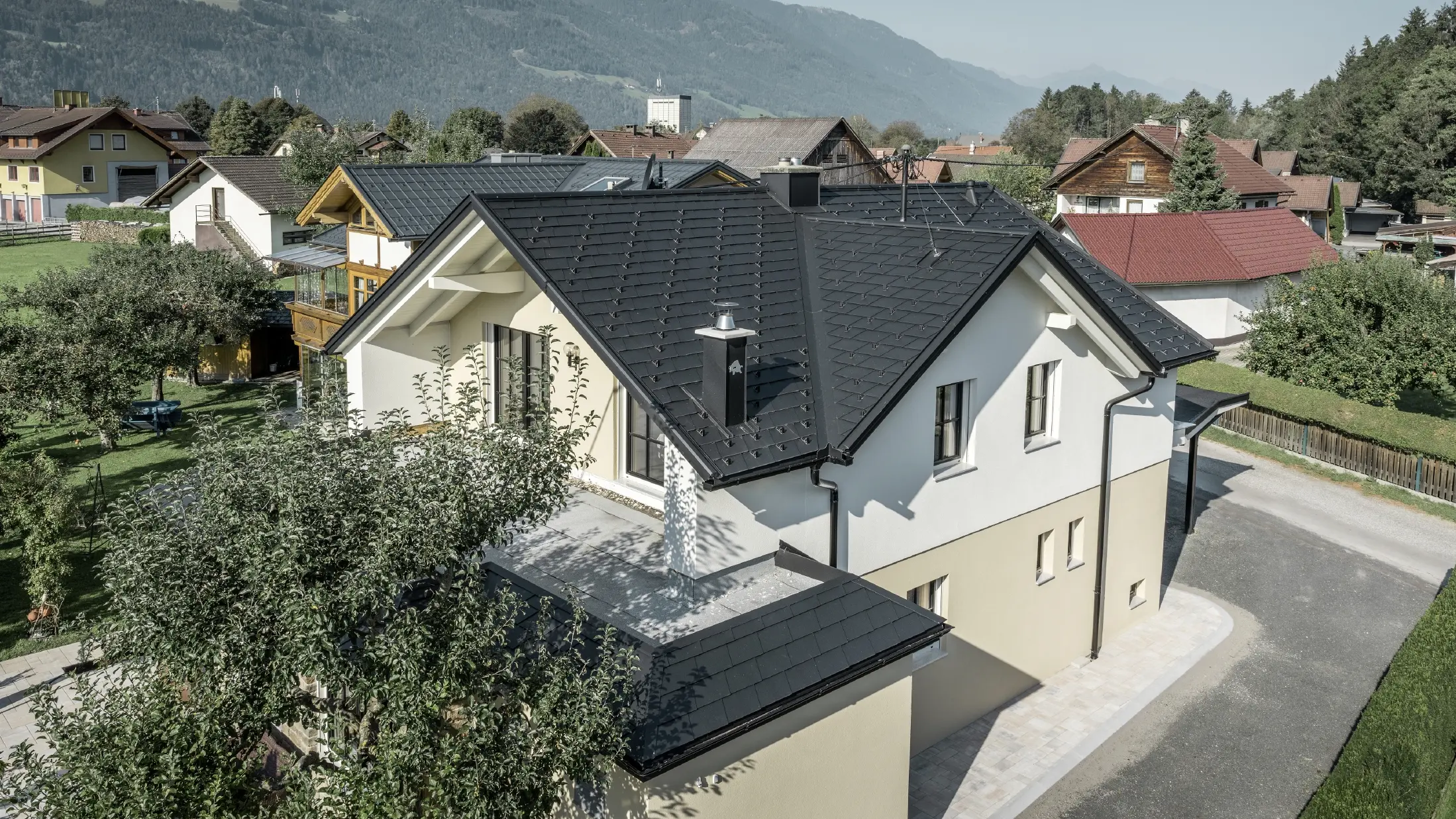 Pohled z ptačí perspektivy na střechu pokrytou falcovanými šindeli a odvodňovací systém PREFA - vše sladěno do barvy P.10 černé