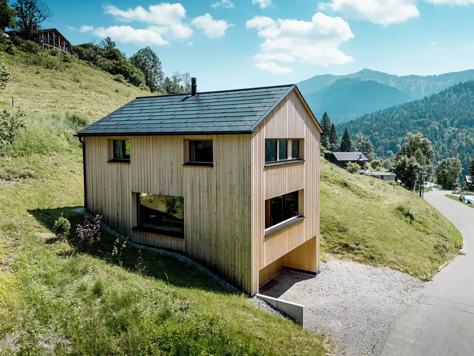 Vysoko nad údolím se na slunném svahu hory Ebnit tyčí dům Haus Immi jako drsný dřevěný monolit. Minimalistická fasáda z bílé jedle a černá solární střecha PREFA vytvářejí výrazný kontrast k rozlehlé alpské krajině. Integrované solární střešní panely a střešní panely R.16 v černé barvě P.10 vyrábějí solární energii, odolávají alpskému počasí a zajišťují dlouhodobý a harmonický vzhled střechy.
