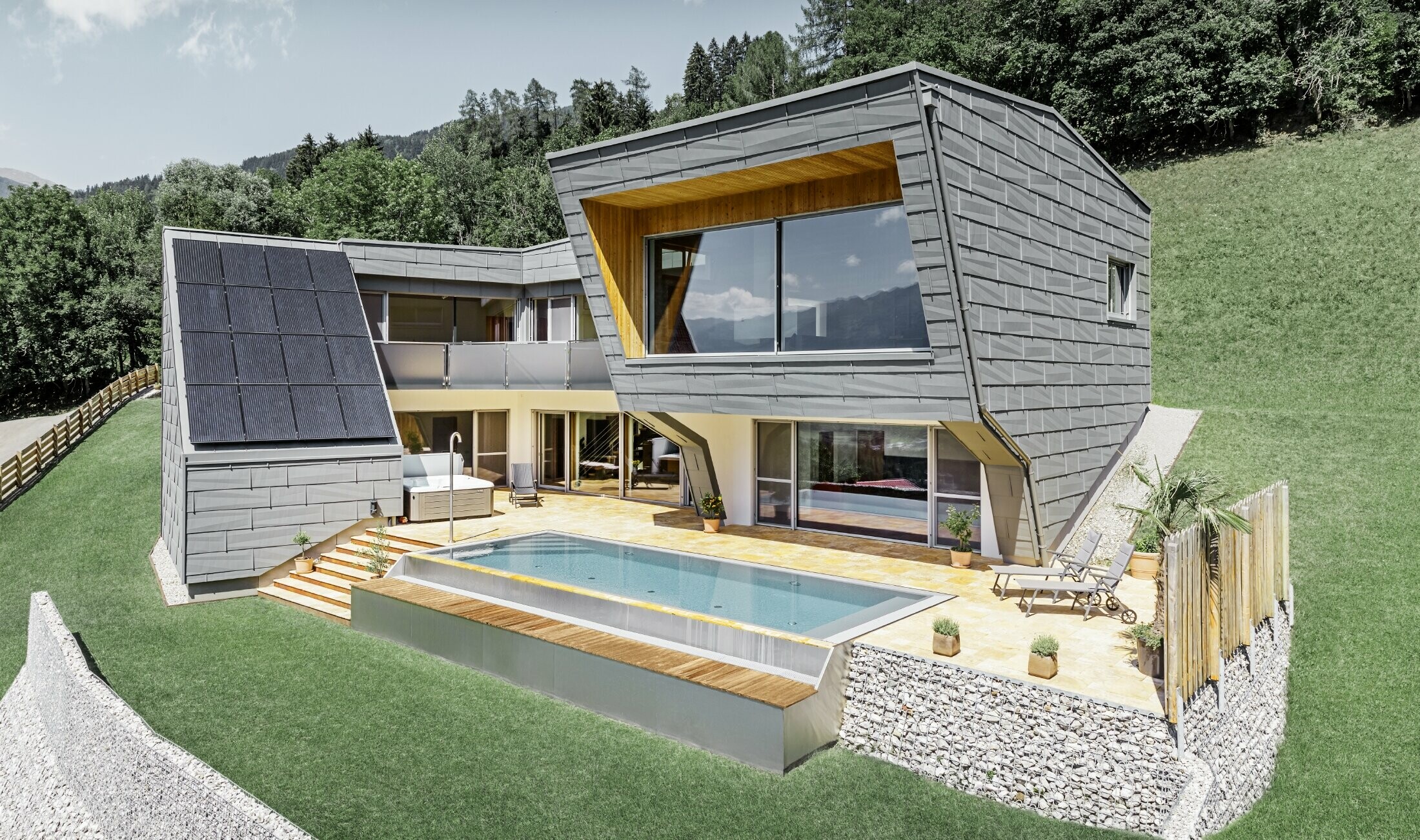 Moderní rodinný dům s bazénem byl postaven na svažitém terénu. Celý dům je opláštěn střešním a fasádním panelem FX.12 od PREFA v barvě P.10. světle šedé