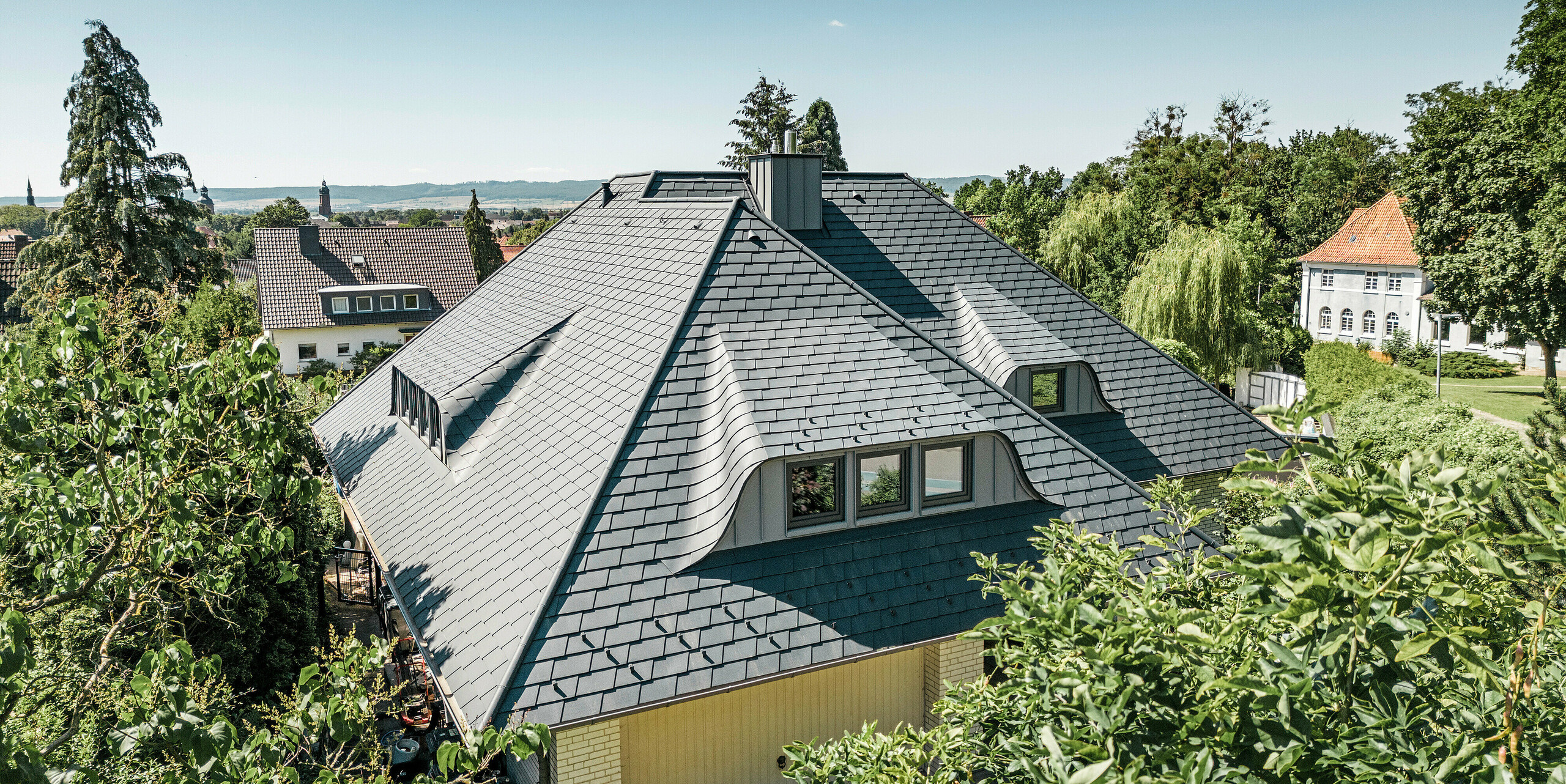 Velká plocha střechy se zakřivenými vikýři na rodinném domě v Einbecku pokrytá falcovanými šindeli PREFA
