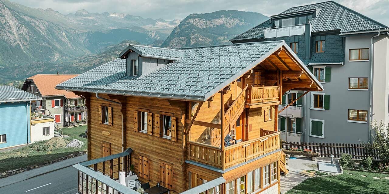Tradiční švýcarská dřevěná chata s vikýřem a sedlovou střechou. Střecha je pokryta falcovanými taškami PREFA v barvě P.10 břidlicové.