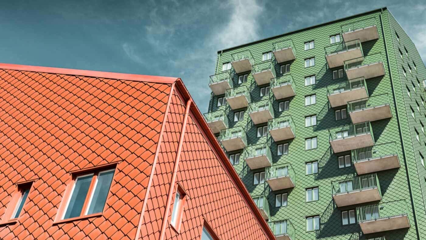 Švédské bytové domy s balkony a PREFA fasádními šablonami v zelené a cihlově červené barvě.
