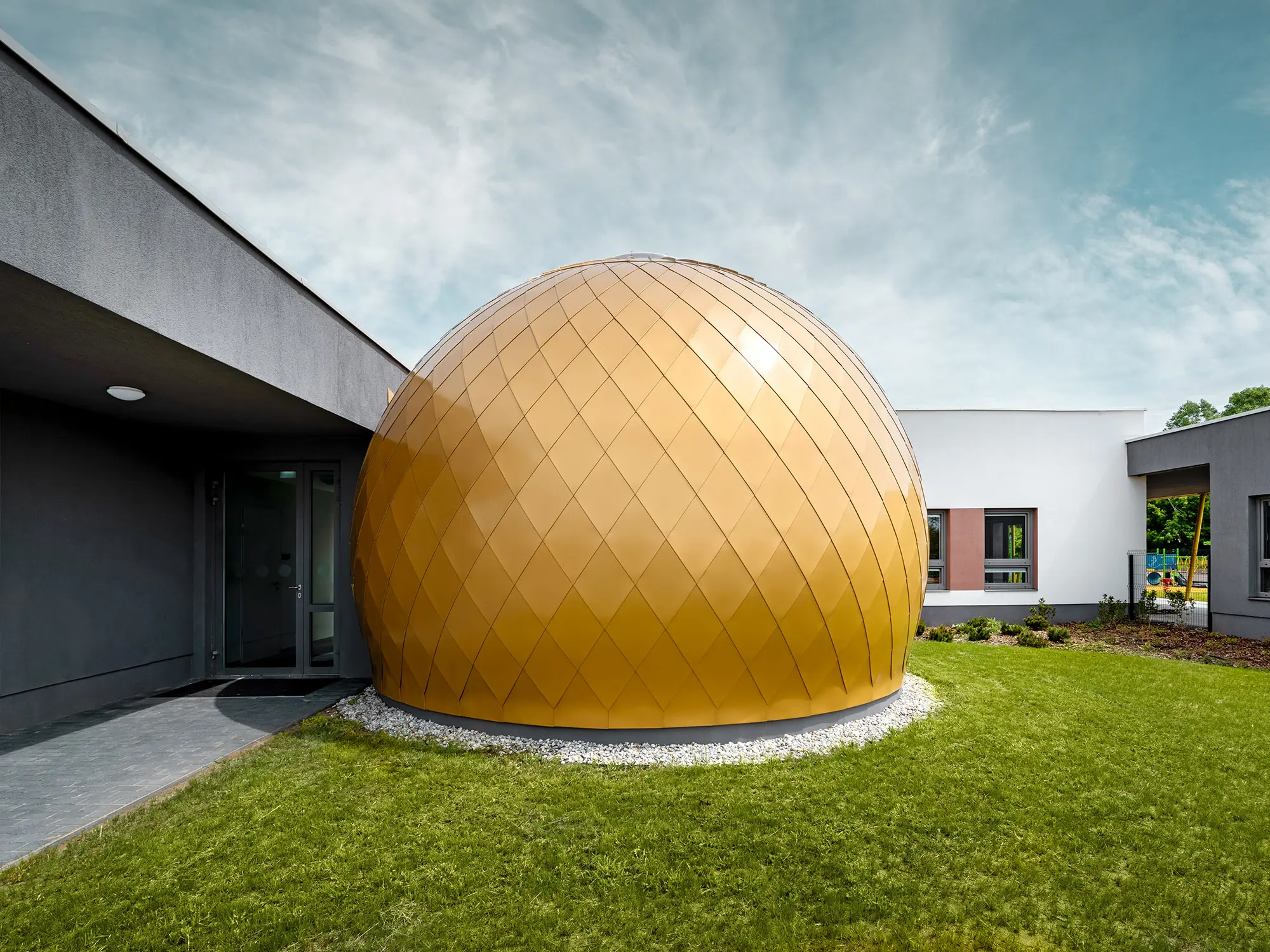Jedna ze tří kulatých místností jeslí navržených architektem László Erdeimem z bočního pohledu, za ní a vedle ní je částečně vidět omítková fasáda budovy a hřiště.