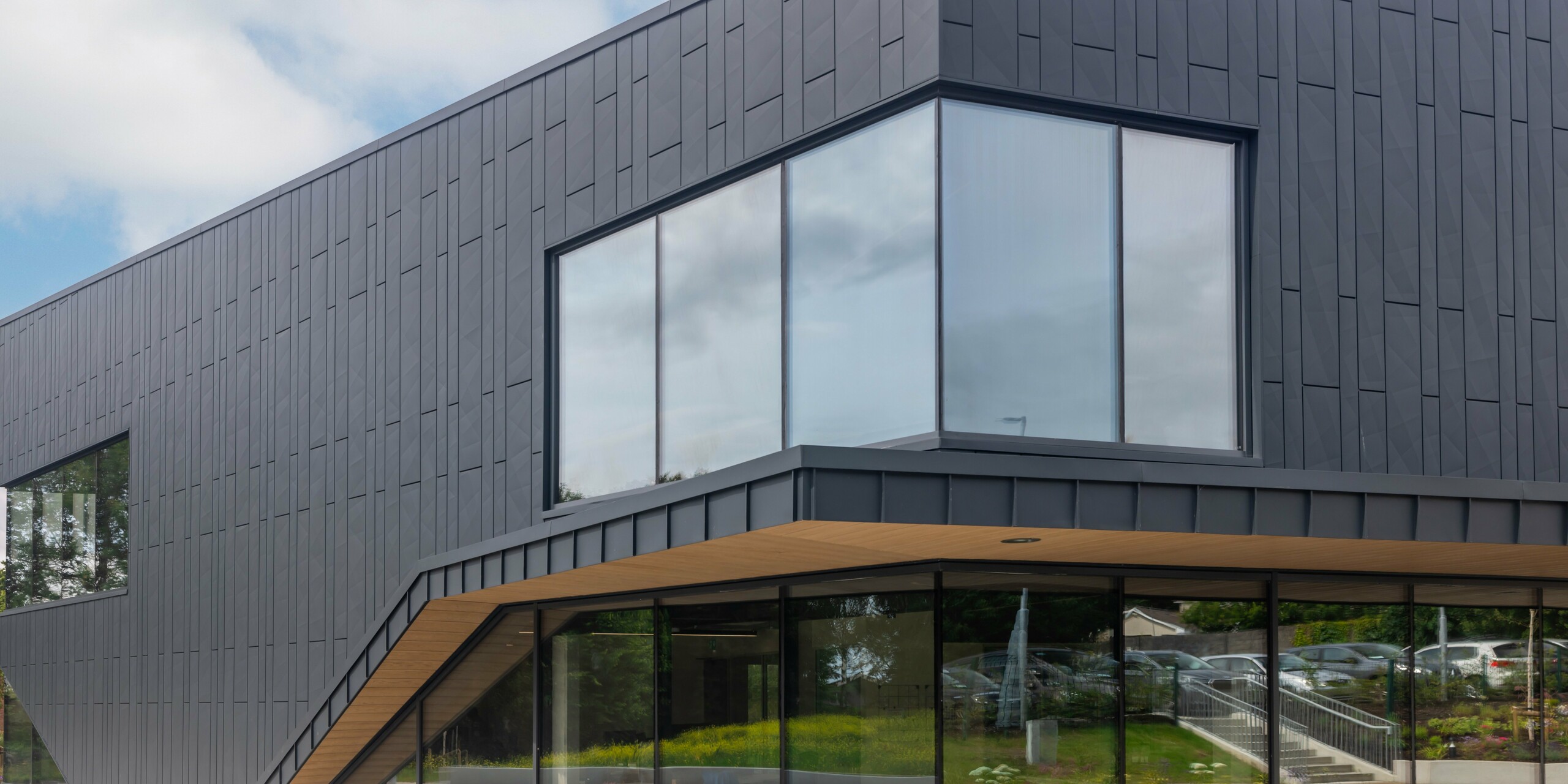 Detailní pohled na moderní fasádu budovy CREW v Galway v Irsku, navrženou fasádními lamely PREFA Siding.X a PREFALZ v barvě P.10 antracitové. Nápadné rohové okno podtrhuje jasné linie a inovativní architekturu budovy. Hliníkové opláštění v antracitové barvě dodává nemovitosti nadčasovou eleganci a dokládá vysokou kvalitu hliníkových výrobků PREFA.