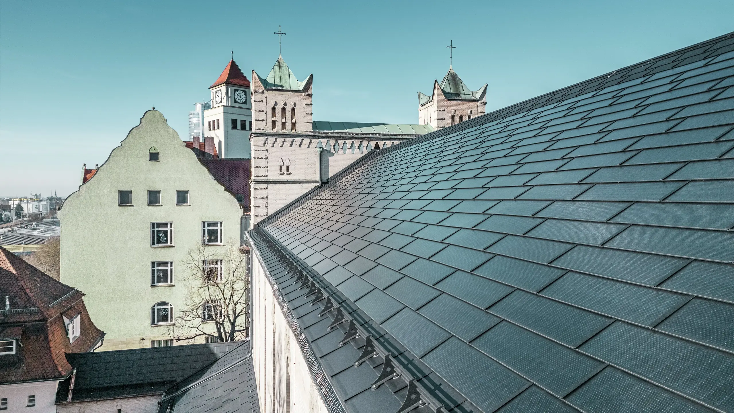 Die Nahaufnahme des Daches der St. Karl Borromäus Kirche in Nürnberg zeigt die präzise verlegten PREFA Solardachplatten in elegantem Schwarz. Die gut integrierten Solarmodule fügen sich harmonisch in die historische Architektur ein und stellen eine nachhaltige Energiequelle dar. Im Hintergrund sind die markanten Kirchtürme mit ihren klassischen spitzen Dächern zu sehen. Die PREFA Dachlösung aus robustem Aluminium verbindet Denkmalschutz mit erneuerbarer Energie perfekt.