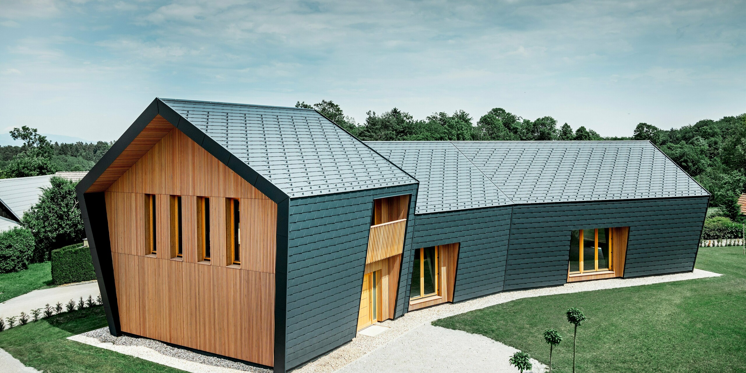 Celkový pohled na boulderingovou halu ve Skofji; Střecha a boční fasáda lezecké haly jsou kompletně opláštěny falcovaným šindelem DS.19 v antracitové barvě od PREFA. Na čelní straně je fasáda obložena modřínovým dřevem světlé barvy.