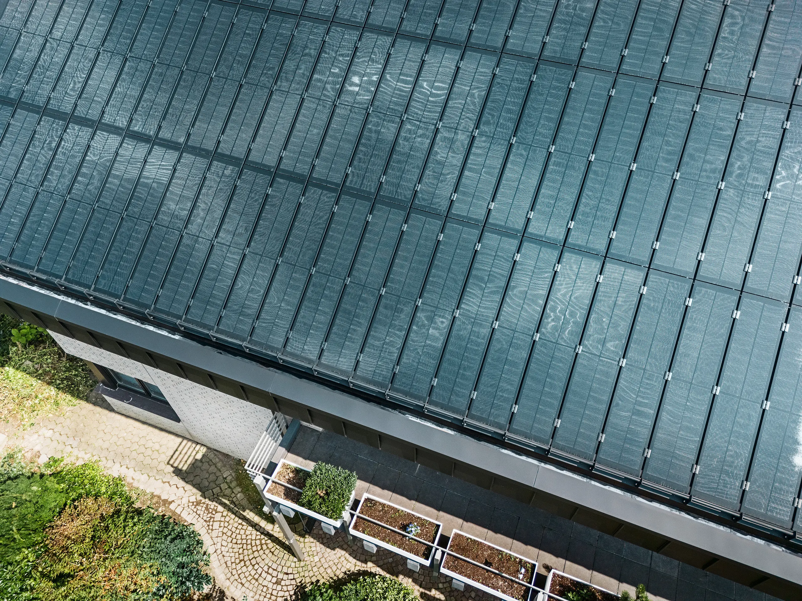 Detailansicht der rahmenlosen Glas/Glas PV-Module mit TOPCon Zelltechnologie auf einer PREFALZ Doppelstehfalzdeckung in P.10 Schwarz. Die spiegelnden Solarmodule unterstreichen das moderne und nachhaltige Design des Einfamilienhauses in Meschede.