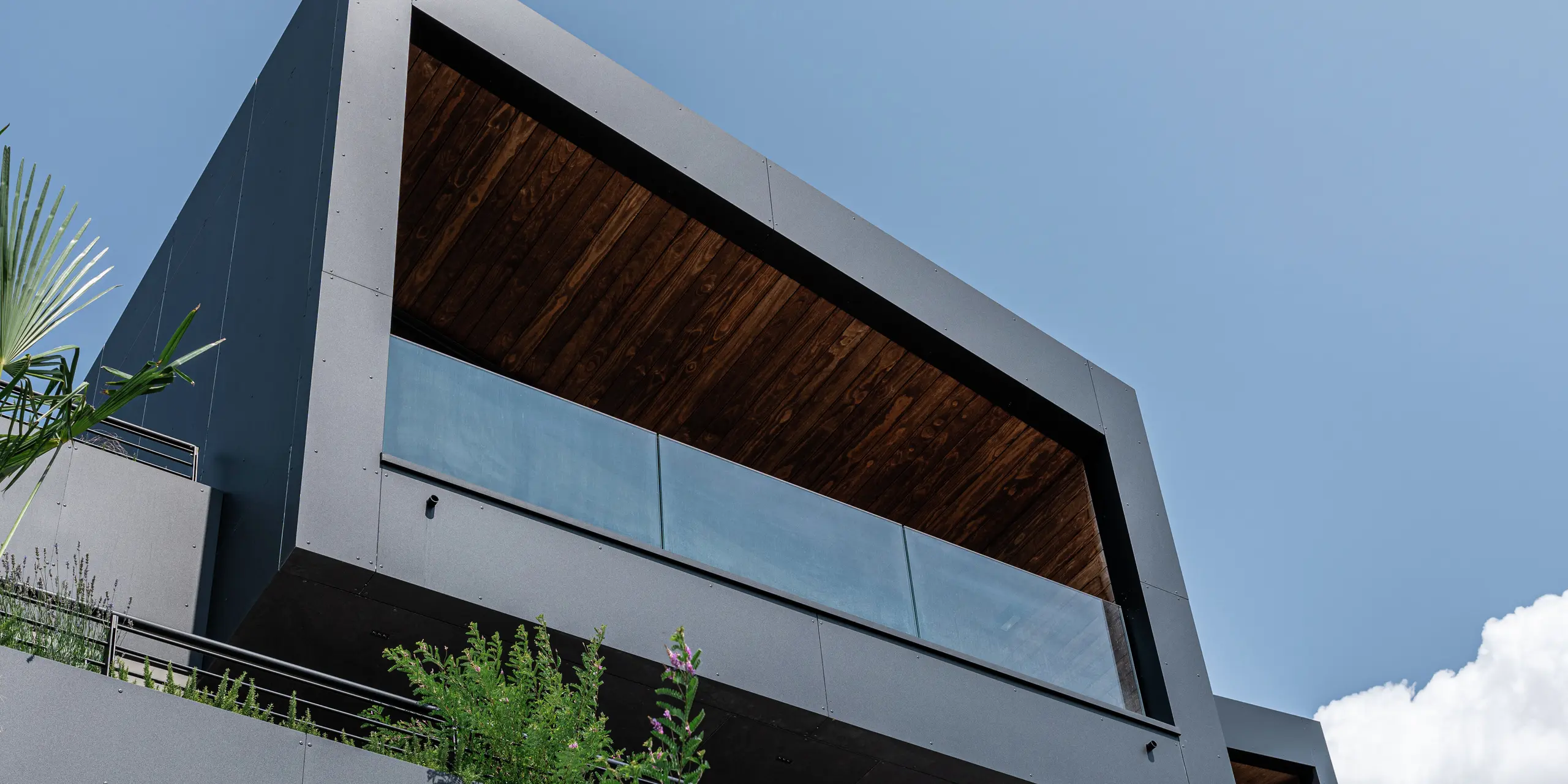 Moderne Architektur trifft auf langlebige Materialien: Die minimalistische Kubusform mit Pultdach und markanter, überdachter Terrasse wird durch die robuste PREFA Aluminiumfassade in P.10 Schwarz perfekt in Szene gesetzt. Die Untersicht betont die klaren Linien und die Widerstandsfähigkeit des Materials, die integrierte Begrünung sorgt für natürliche Harmonie. Witterungsbeständig, pflegeleicht und stilvoll - die PREFA Gebäudehülle garantiert Schutz und Beständigkeit in jeder Situation.
