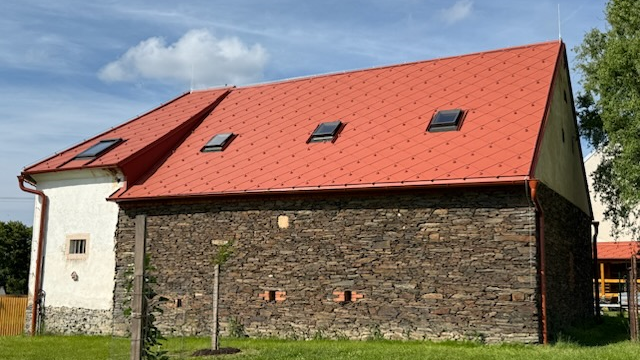 Objekt s novou střešní krytinou PREFA a původním kamenným zdivem, na které navazuje bílá omítka.