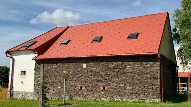 Objekt s novou střešní krytinou PREFA a původním kamenným zdivem, na které navazuje bílá omítka.