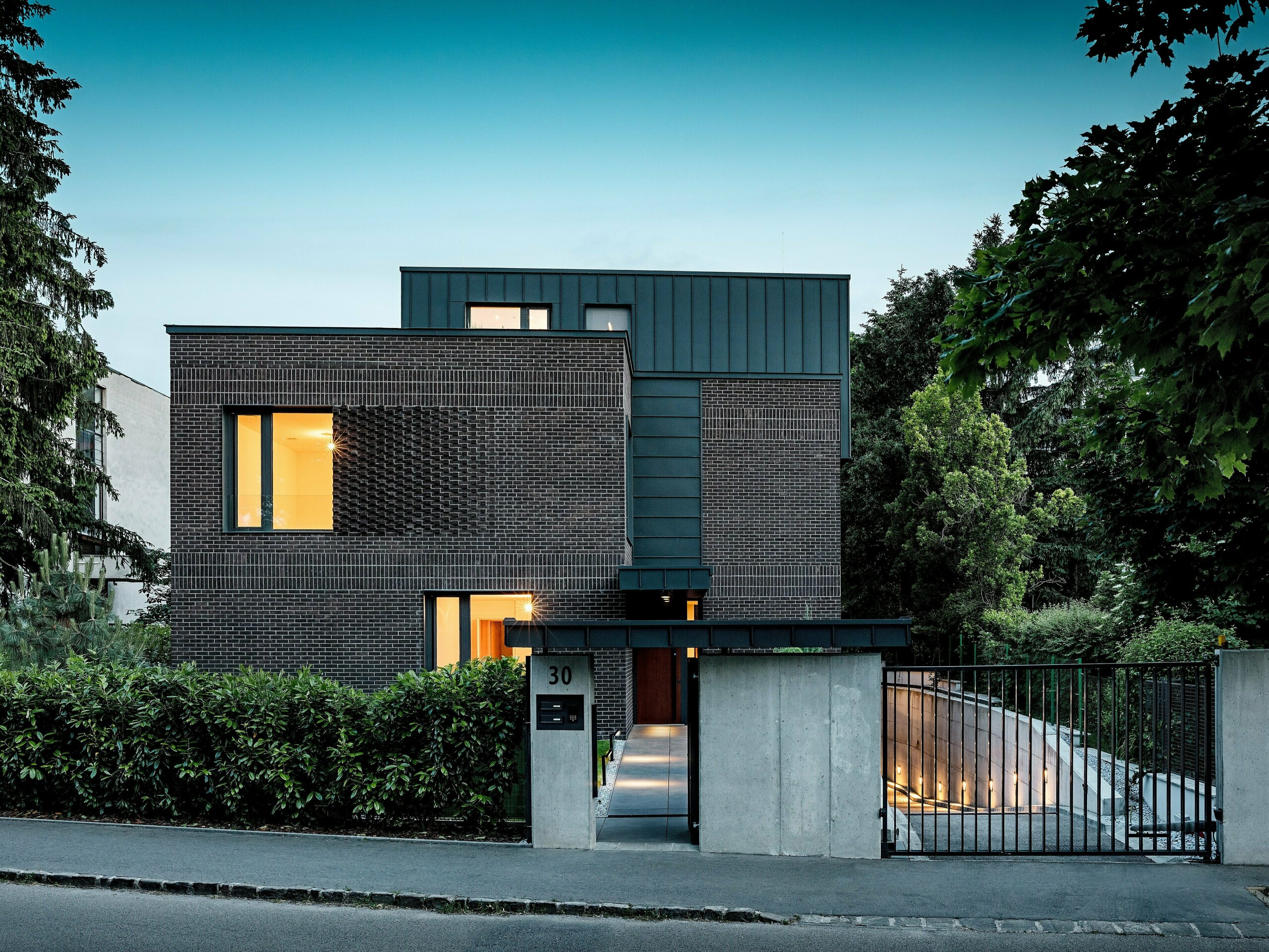 Na obrázku je moderní bytový dům v Budapešti, jehož kubická střešní konstrukce obložená hliníkem PREFALZ v antracitové barvě P.10 vytváří výrazný kontrast s historickým okolím. Svislé stojaté drážky vytvářejí podmanivou hru světla a zdůrazňují čisté linie architektury. Vysoce kvalitní hliníkové výrobky PREFA nejenže dodávají budově elegantní a nadčasový vzhled, ale také přesvědčují svou trvanlivostí, odolností vůči povětrnostním vlivům a precizním zpracováním. Antracitově zbarvená fasáda a střešní plocha působí jako silný poutač a podtrhují inovativní charakter budovy.