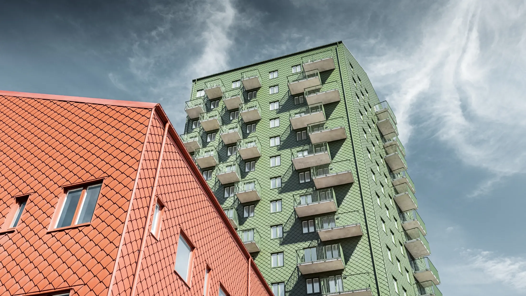 Výškové budovy s balkony s fasádním řešením pomocí PREFA fasádních šablon 29 × 29 v olivově zelené a cihlově červené barvě