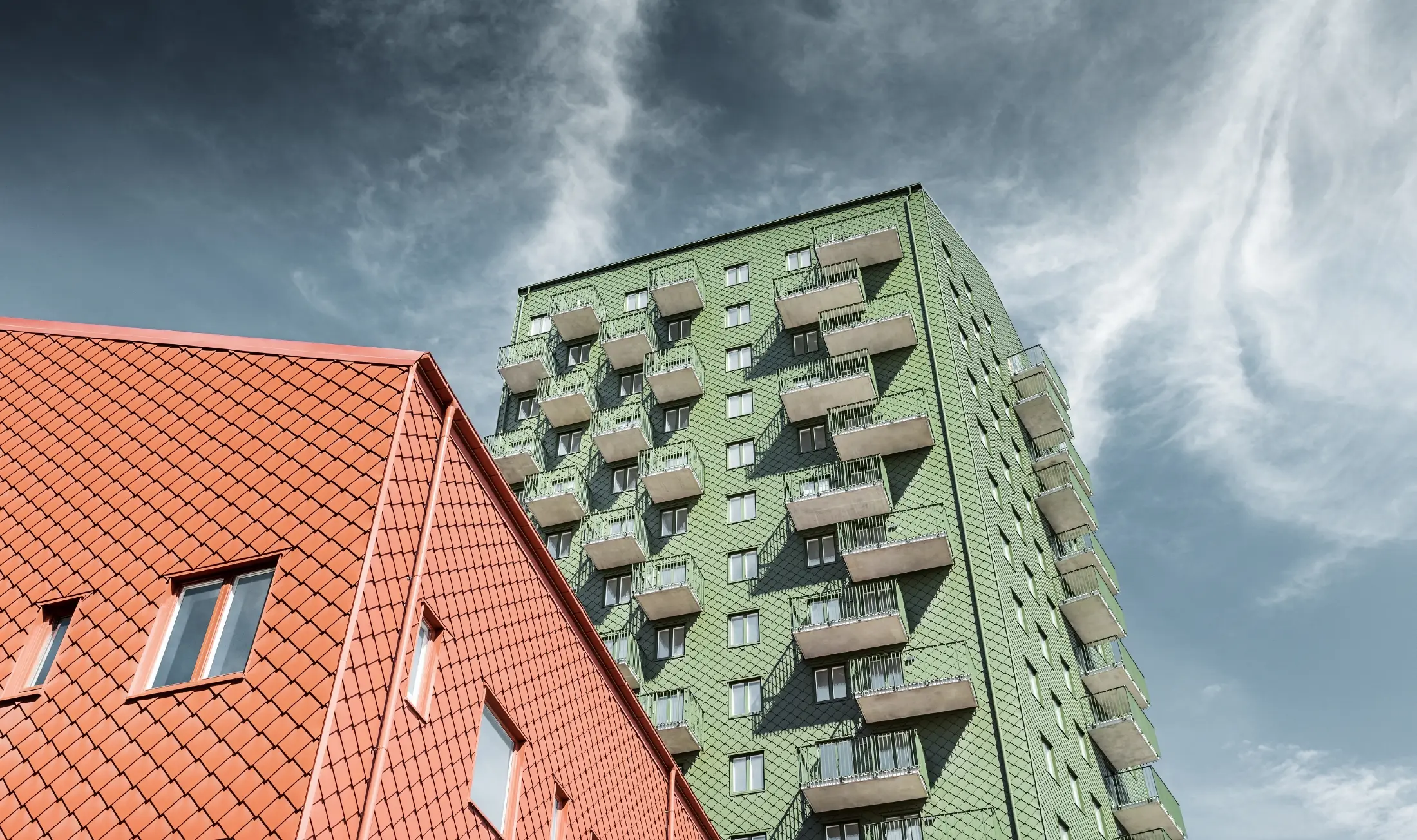 Výškové budovy s balkony s fasádním řešením pomocí PREFA fasádních šablon 29 × 29 v olivově zelené a cihlově červené barvě