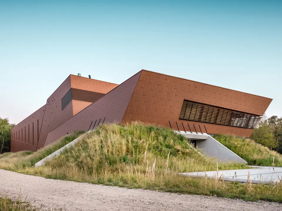 Architektonicky expresivní čerpací stanice pitné vody WML v Lottum se vyznačuje sochařsky skládanými tvary budov, zasazenými do přírodní krajiny nábřeží. Výrazná hliníková fasáda PREFA Siding.X s teplým, rezavějícím vzhledem a fazetovaným, zářivým povrchem je skutečným poutačem a vytváří působivou hru světla a stínu. Horizontální žaluzie a přesné linie zdůrazňují dynamickou geometrii. Lehké, trvanlivé a plně recyklovatelné hliníkové panely PREFA nabízejí maximální odolnost proti povětrnostním vlivům, udržitelnou konstrukci a nenáročný na údržbu pláště budovy.