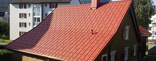 Sedlová střecha v cihlově červené barvě pokrytá  PREFA falcovanými hliníkovými střešními taškami se sněhovými zarážkami a komínem 