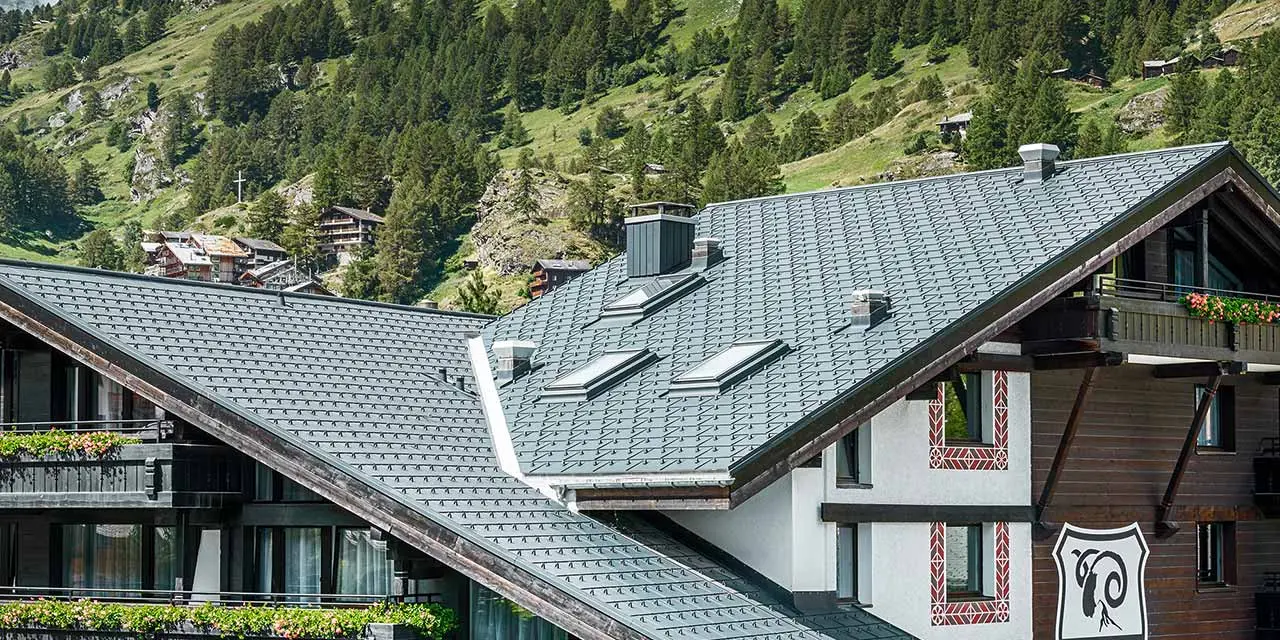 Hotel Alpenhof v Zermattu s Matterhornem v pozadí, balkony s tmavou dřevěnou fasádou a hliníkovou střechou PREFA v antracitové barvě