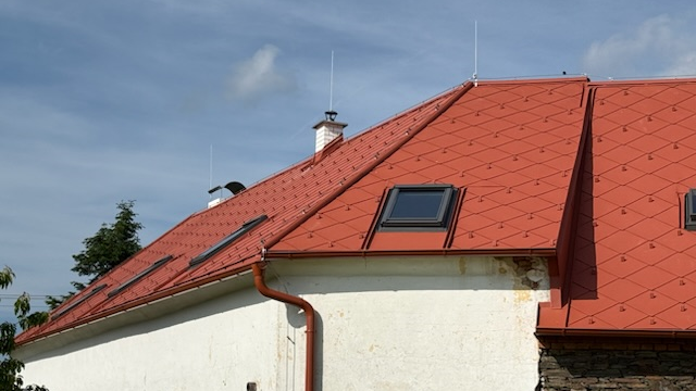 Střešní nároží, lemování oken a falcovaná šablona 44 x 44 ve tvaru kosočtverce v barvě P.10 tmavě červené zachovává kontinuitu původní krytiny.