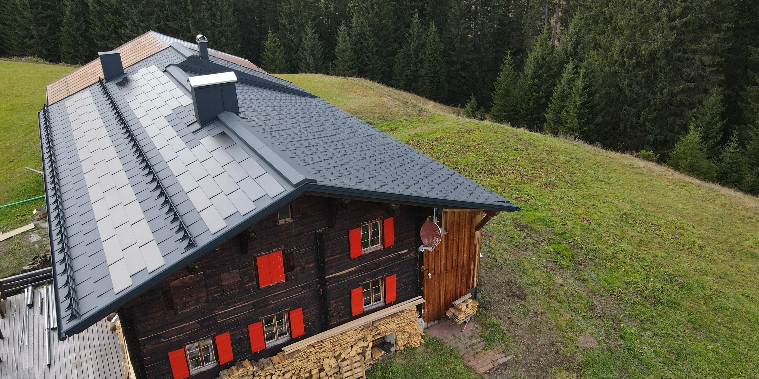 Starý dům s dřevěnou fasádou, červenými okenicemi a hliníkovou střechou doplněnou o protisněhové prvky