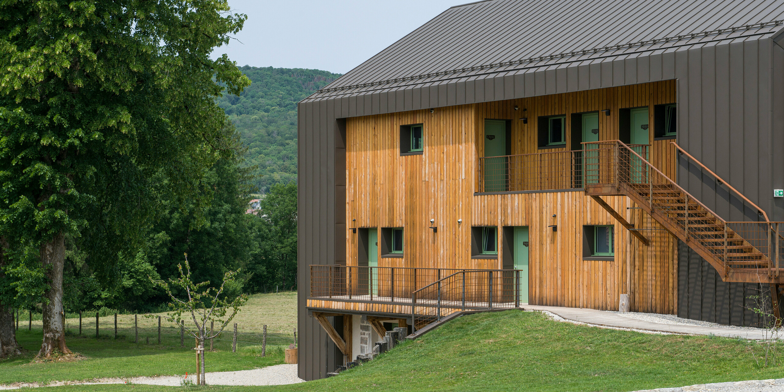 Boční pohled na budovu hotelu, který má kombinovanou fasádu ze dřeva a hliníku PREFALZ a střechu pokrytou PREFALZ v barvě P.10 tmavě hnědé. Střecha je vybavena také protisněhovými prvky od PREFA.