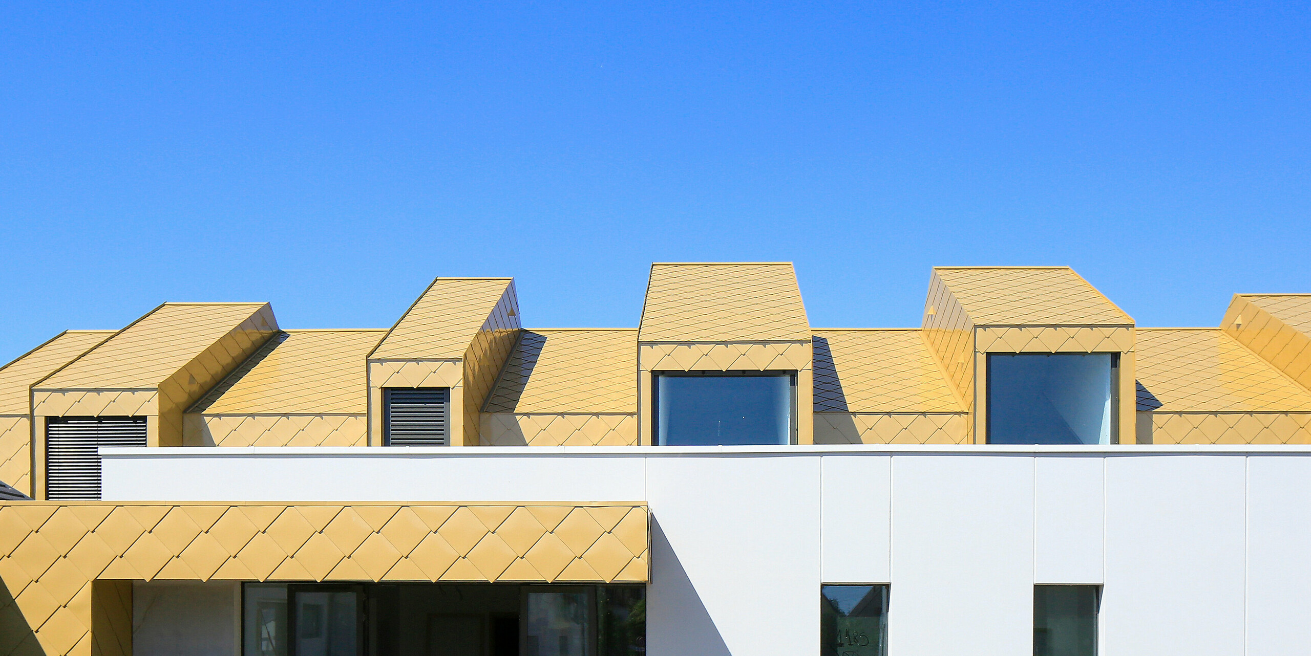 Střecha a fasáda nejvyššího patra v Komunitním a kulturním centru Fessenheim ve Francii byly pokryty PREFA falcovanými a fasádními šablonami 44 × 44 v jiskřivém zlatě na přání.