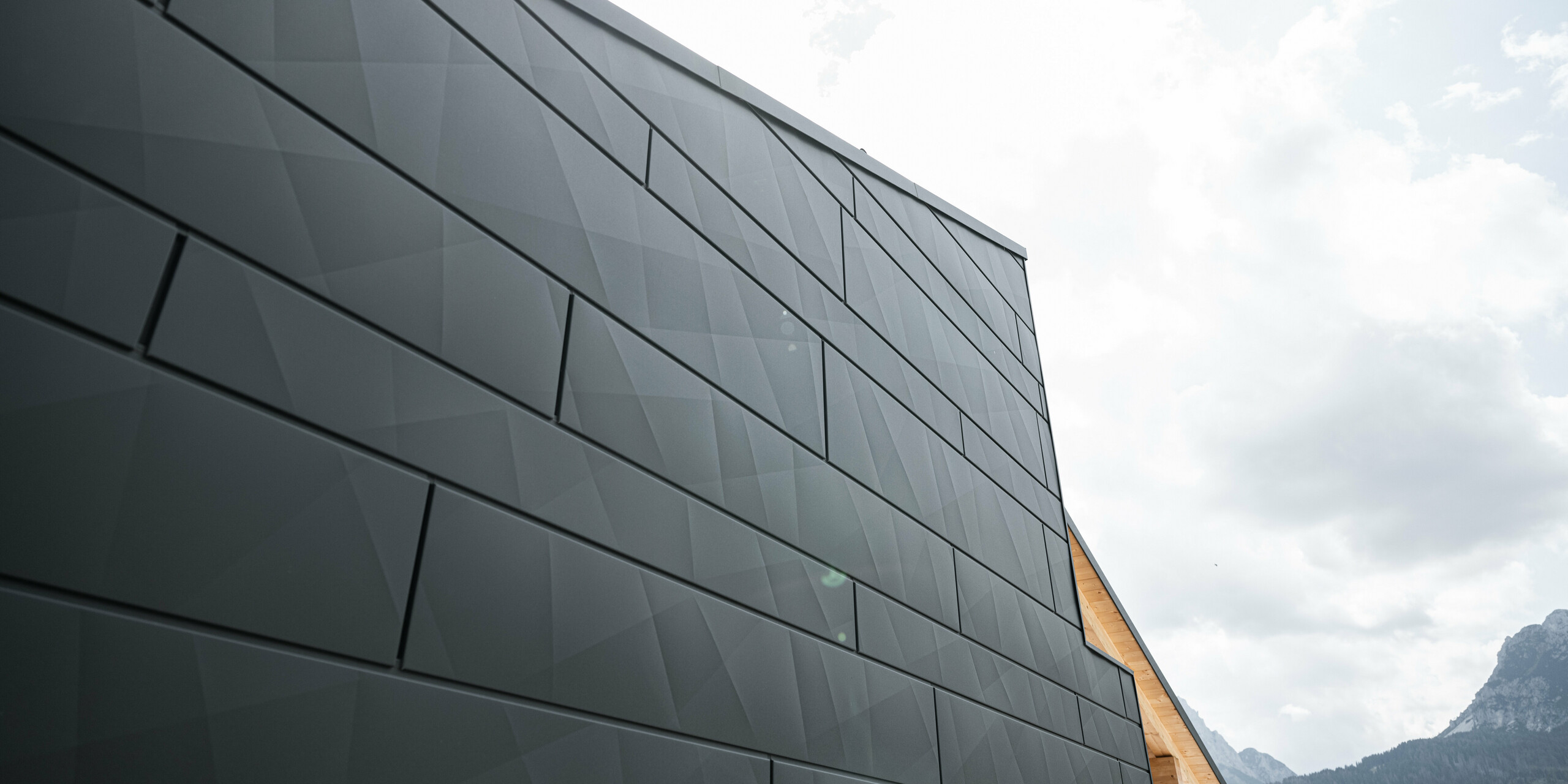 Detailaufnahme der PREFA Siding.X Fassadenpaneele in P.10 Schwarz am Casa Hoffe in Sappada, Italien. Die Paneele aus Aluminium präsentieren ein modernes, geometrisches Muster, das der Struktur eine zeitgenössische Textur verleiht, während es sich harmonisch in die alpine Umgebung einfügt. Dieses Bild zeigt die Innovation und Qualität von PREFA, die eine ästhetische und dauerhafte Verkleidung für moderne Architektur bereitstellt.