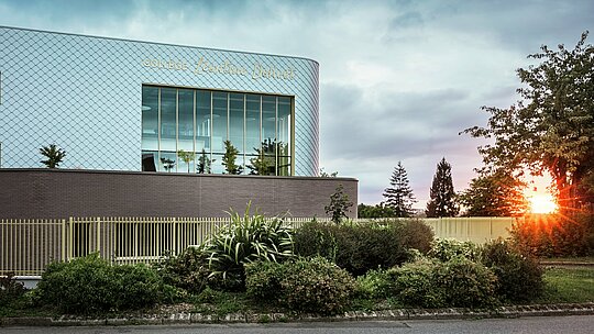 Modernes Schulgebäude Collège Léontine Dolivet in Cesson-Sévigné mit markanter Aluminiumfassade aus rund 15.000 PREFA Wandrauten in Silbermetallic. Die schimmernde Oberfläche reflektiert das Licht und erzeugt ein lebendiges, elegantes Erscheinungsbild. Große Glasfronten öffnen den Blick ins Grüne, während die robuste PREFA Fassadenlösung Langlebigkeit und Witterungsbeständigkeit garantiert. Die Kombination aus changierendem Metall und klarer Architektur macht das Gebäude zu einem echten Eyecatcher und unterstreicht die Vorteile von Aluminium: leicht, wartungsfrei und nachhaltig.