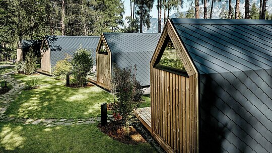 Série minimalistických domků v Secret Koi Garden se nachází v dobře udržované zelené ploše u jezera Natterer. Šikmé střechy a fasády jsou obloženy drobnými hliníkovými kosočtverci PREFA v antracitové barvě P.10, které vytvářejí klidnou texturu připomínající rybí šupinky. Trvanlivé a povětrnostním vlivům odolné hliníkové povrchy PREFA, obklopené stromy a keři, nabízejí optimální ochranu a propůjčují glampingovému resortu jasný, nadčasový architektonický jazyk v harmonii s přírodou.