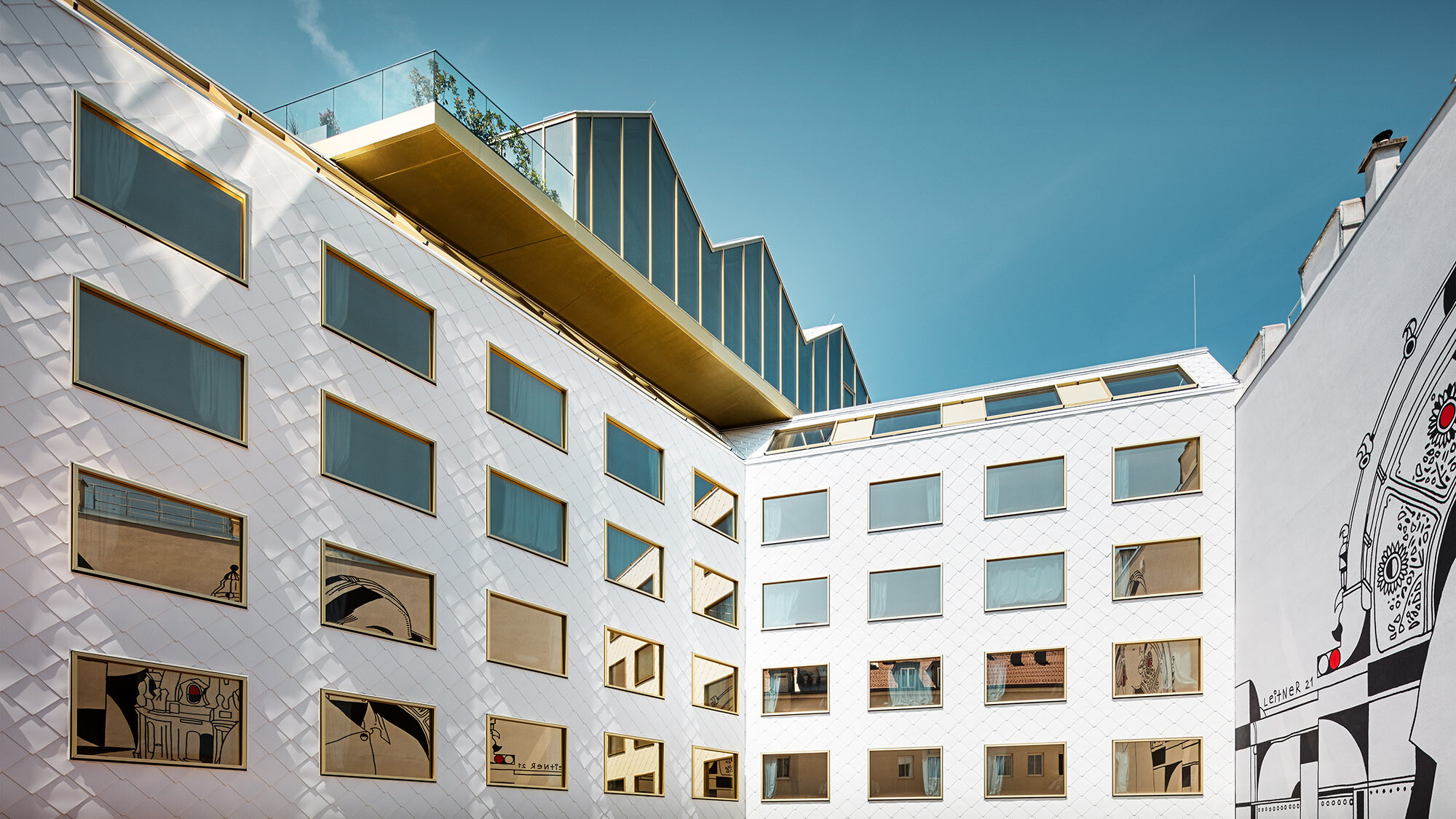 Pohled na hotel ze dvora; kus nástěnného umění se odráží v oknech, střešní bar mírně převyšuje hotel.