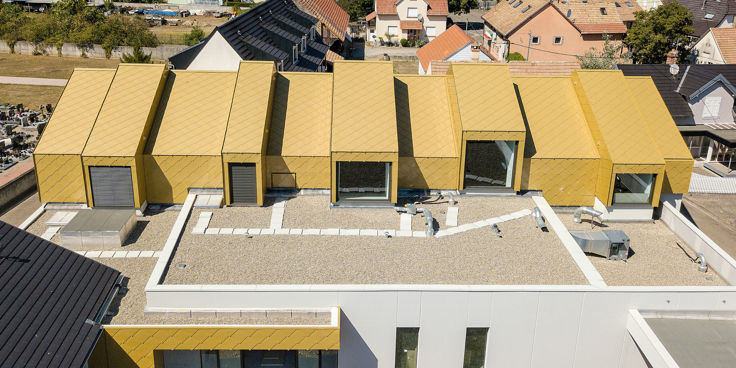 Pohled z ptačí perspektivy na střechu komunitního a kulturního centra Fessenheim ve Francii. Střecha a části fasády byly pokryty falcovanými a fasádními šablonami 44 × 44 v jiskřivé zlatě na přání.
