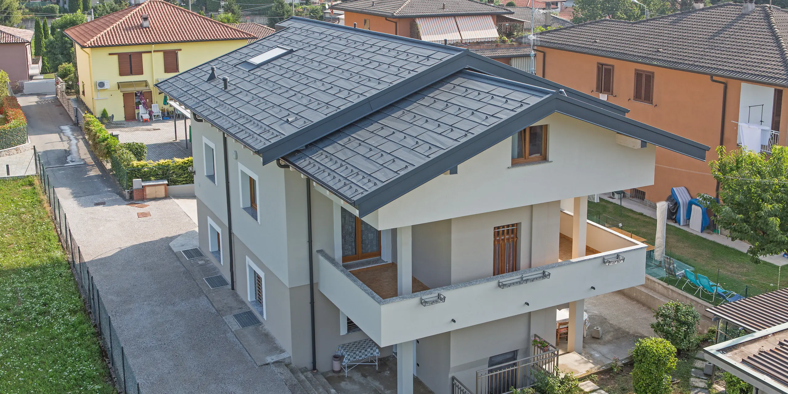 Detailaufnahme des PREFA Dachs FX.12 in P.10 Anthrazit auf einem Einfamilienhaus in Beregazzo, Italien. Die markanten, unregelmäßig gekanteten Aluminium-Dachpaneele erzeugen ein faszinierendes geometrisches Muster und ein dynamisches Lichtspiel. Die elegante Dachfläche vereint moderne Architektur mit den Vorteilen von PREFA Aluminium: langlebig, witterungsbeständig und optisch außergewöhnlich.