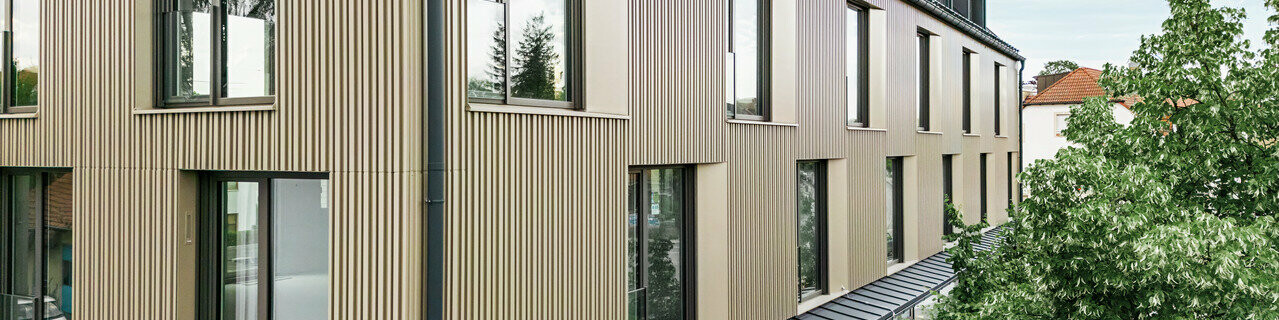 Na obrázku je moderní budova ve Feldkirchu, kterou navrhl architekt Stefan Heigl. Fasáda je vyrobena z Prefalz v barvě bronz a sedlová střecha je pokryta Prefalz v černo-šedé. Velká okna poskytují dostatek světla uvnitř, zatímco prosklená část přízemí nabízí příjemný jídelní kout. Výběr kvalitních materiálů a elegantní design dodávají budově moderní a stylový vzhled.
