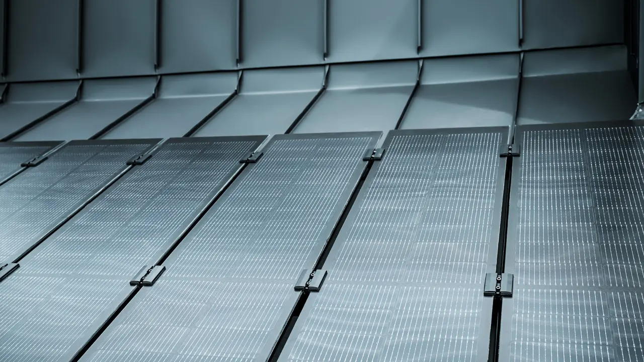 Detailaufnahme einer modernen PREFALZ Dachfläche mit integrierten Solarmodulen. Die rahmenlosen Glas/Glas-PV-Module mit innovativer TOPCon-Zellentechnologie fügen sich nahtlos in das elegante Aluminiumdach ein und sorgen für eine ästhetische, homogene Optik. Die dunkle Oberfläche reflektiert das Licht dezent und unterstreicht das hochwertige Design. Dank flacher Neigung profitieren die Module von einem verbesserten Selbstreinigungseffekt, was langfristig maximale Effizienz und geringen Wartungsaufwand garantiert – eine perfekte Kombination aus Nachhaltigkeit, Leistung und Design.