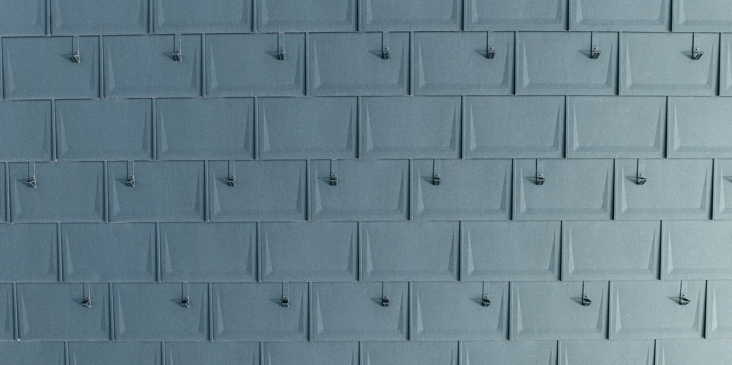 Detailansicht der präzise verlegten PREFA Dachplatten R.16 in P.10 Anthrazit mit montierten Schneestoppern. Die geradlinige Dachplatte aus Aluminium überzeugt durch moderne Optik, Langlebigkeit und extreme Witterungsbeständigkeit. Durch die ausgeklügelte Befestigungstechnik ist sie besonders sturm- und bruchsicher. Die Schneestopper sorgen für zusätzliche Sicherheit in schneereichen Regionen und verhindern ein unkontrolliertes Abrutschen der Schneemassen.