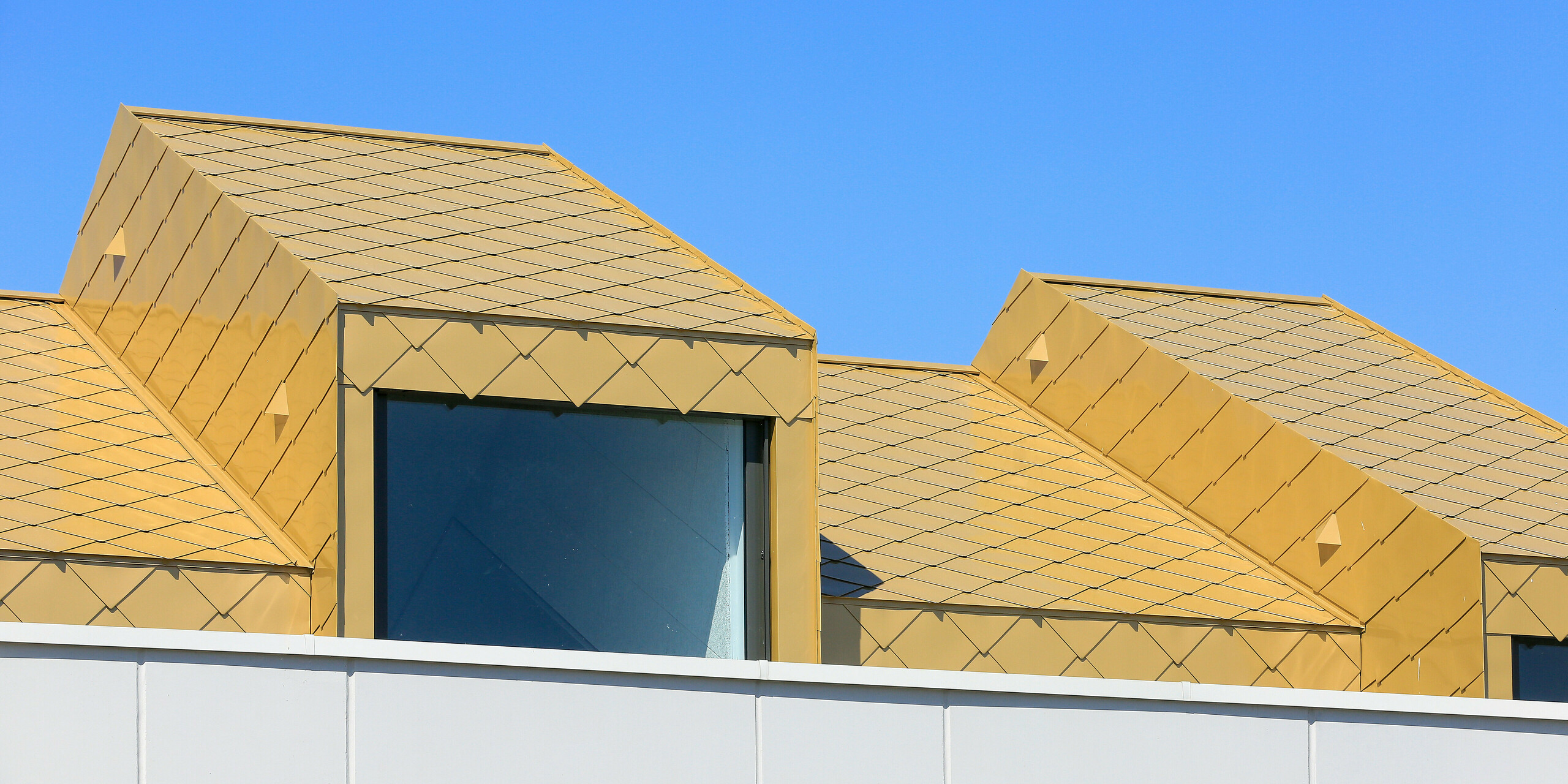 Detail na oplechování vikýře, který je vetknut do střechy, která je opláštěna zlatými hliníkovými šablonami 44 × 44 v barvě na přání - Sparkling Gold.
