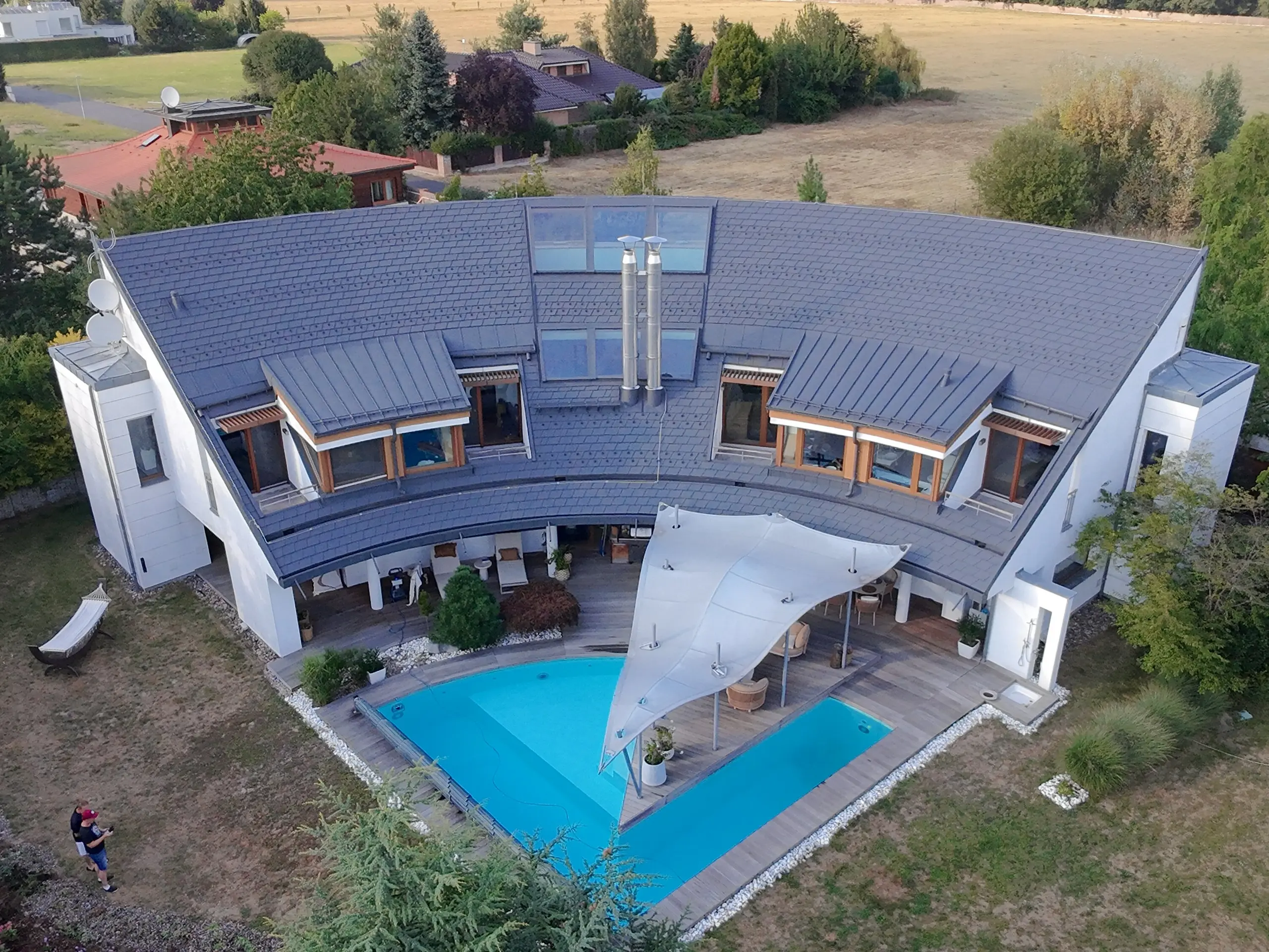 Pohled z dronu na celou vilu s bazénem a atypickou zakřivenou střechou z PREFA produktů sladěných v tmavě šedé