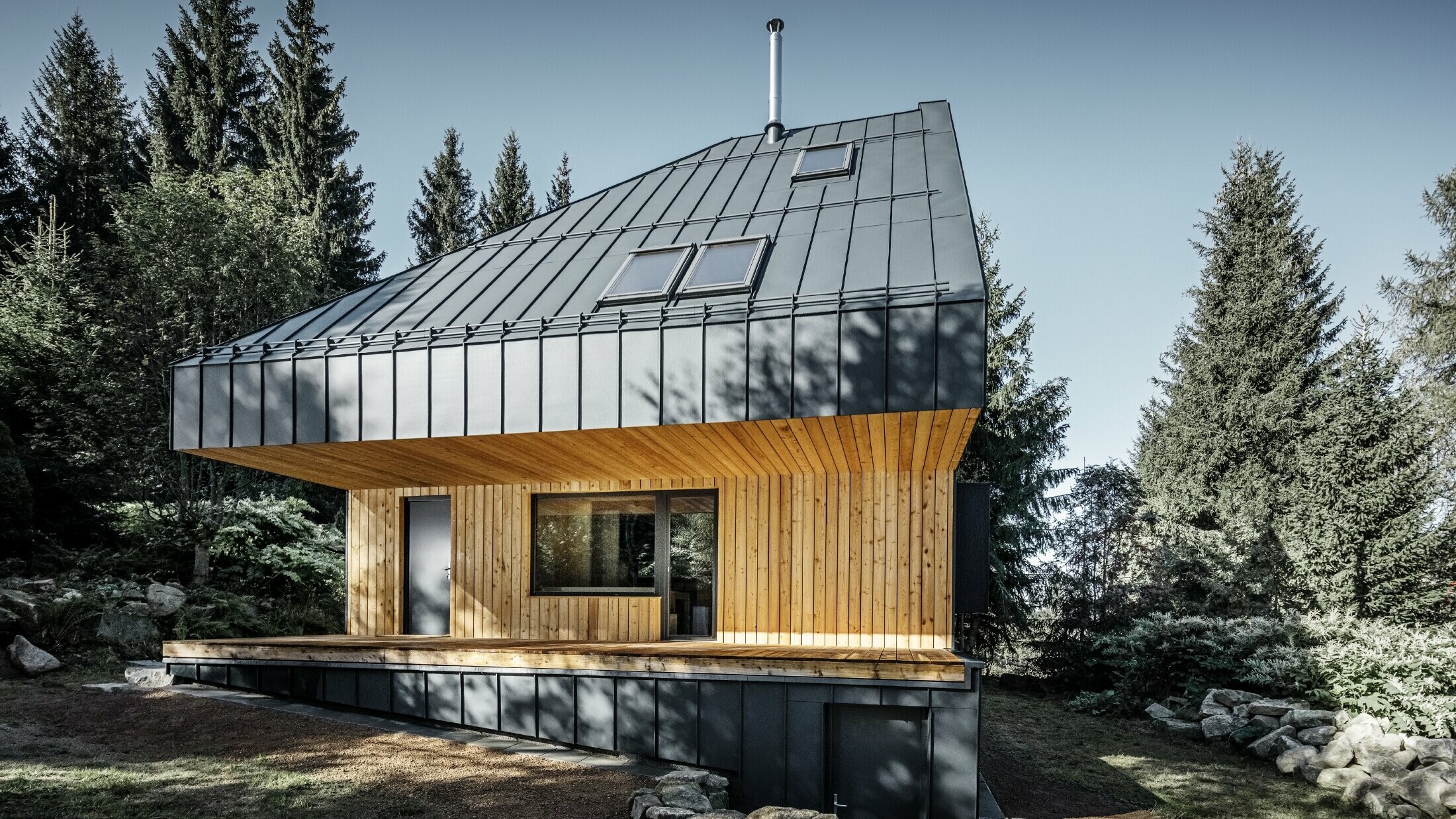 Architektonický rodinný dům v lese, impozantní střecha byla opláštěna drážkovou krytinou PREFALZ v antracitové barvě. Podhled a fasáda jsou obloženy dřevěnými panely.