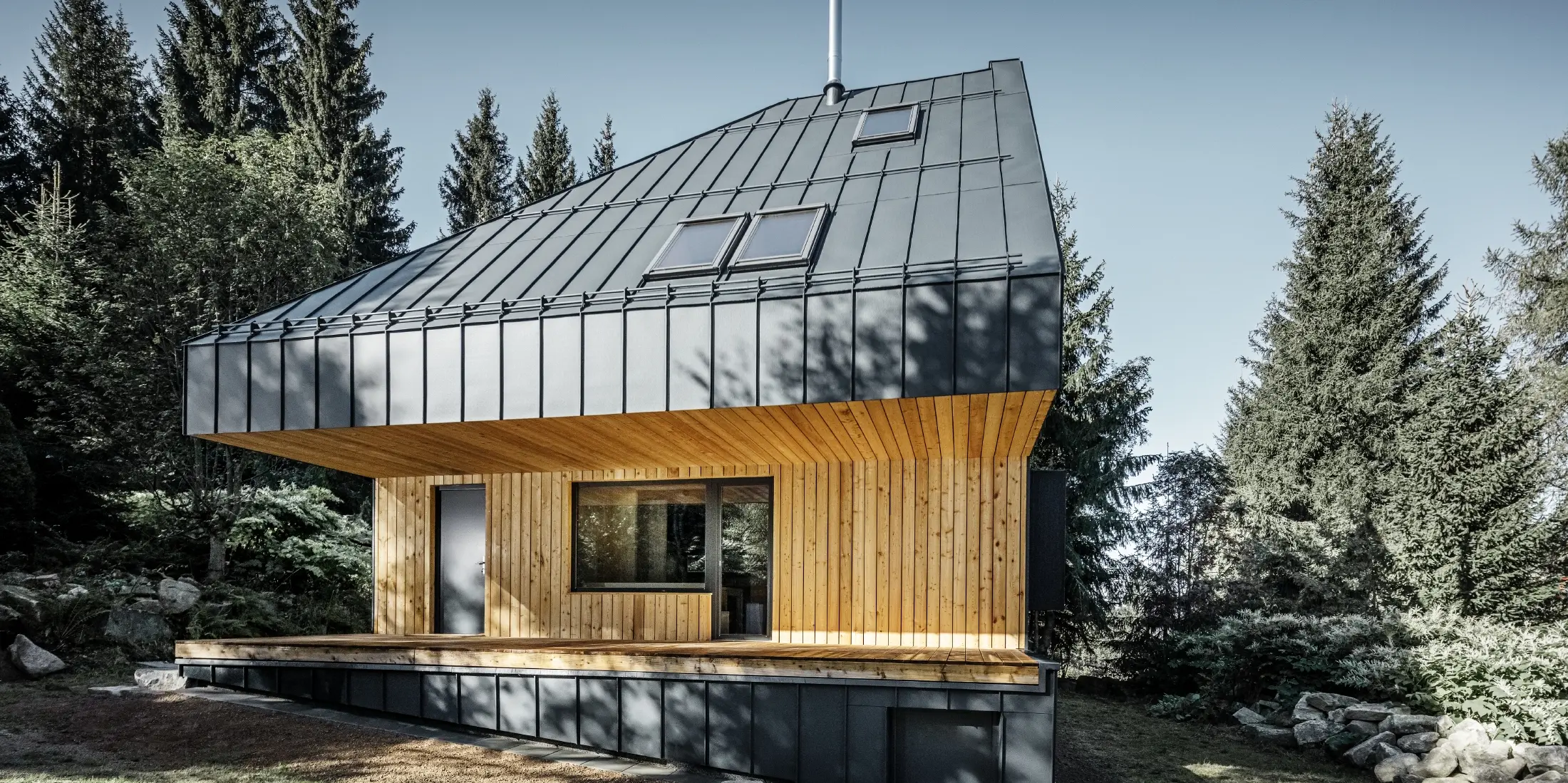 Architektonický rodinný dům v lese, impozantní střecha byla opláštěna drážkovou krytinou PREFALZ v antracitové barvě. Podhled a fasáda jsou obloženy dřevěnými panely.