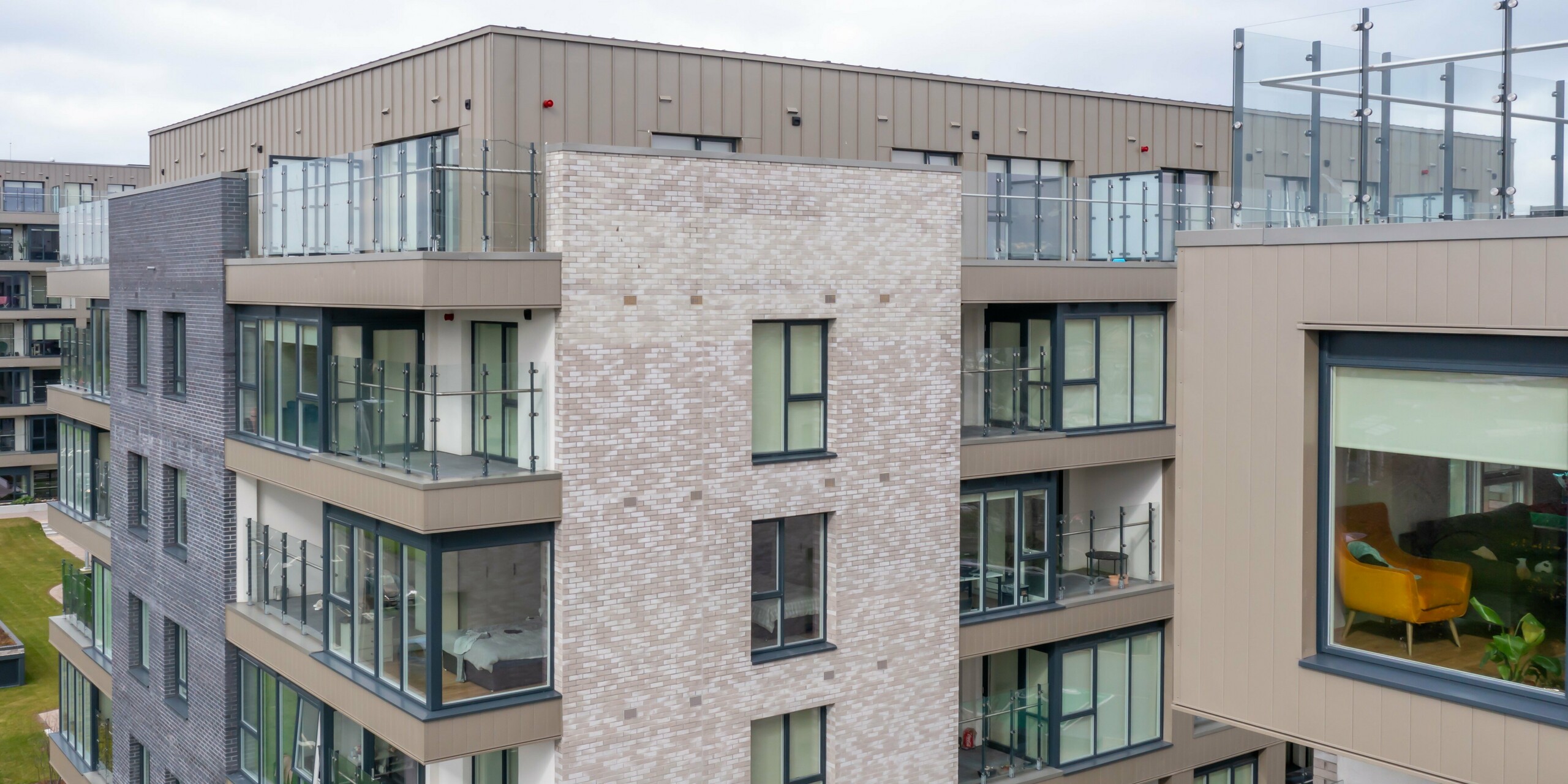 Záběr z dronu na rezidenční komplex Palmers Gate v Palmerstown, Dublin, Irsko - Detailní pohled na obytnou budovu oděnou bronzovými fasádními systémy PREFA. Jedná se o kombinaci fasádních lamel Siding a drážkované krytiny PREFALZ,  které jsou vyhledávané pro svou dlouhou životnost, odolnost a moderní design.