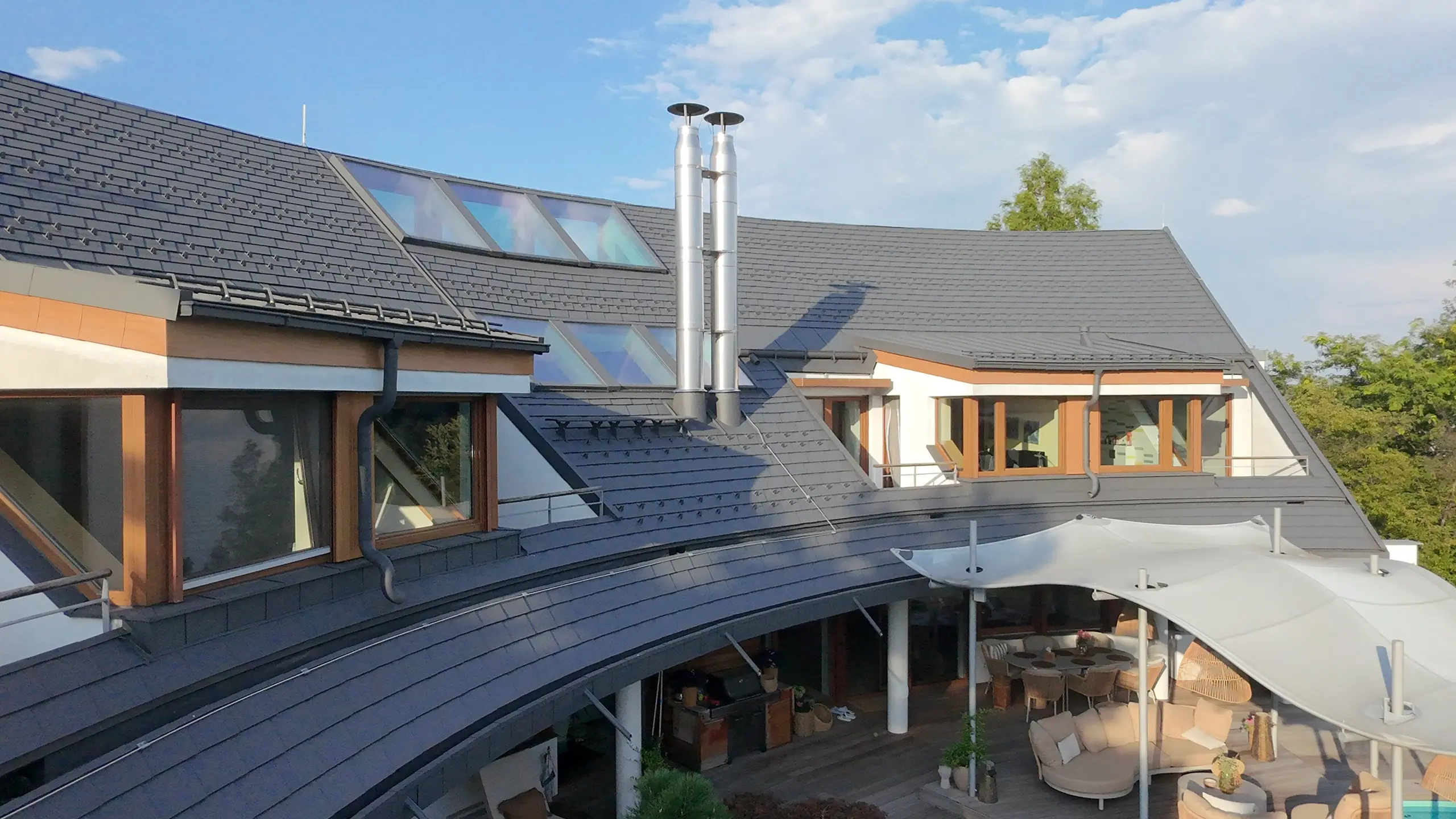 Atypický střešní plášť s proměnlivým rádiusem a výrazným zakřivením s novou krytinou z PREFA falcovaných šindelů v P.10 tmavě šedé