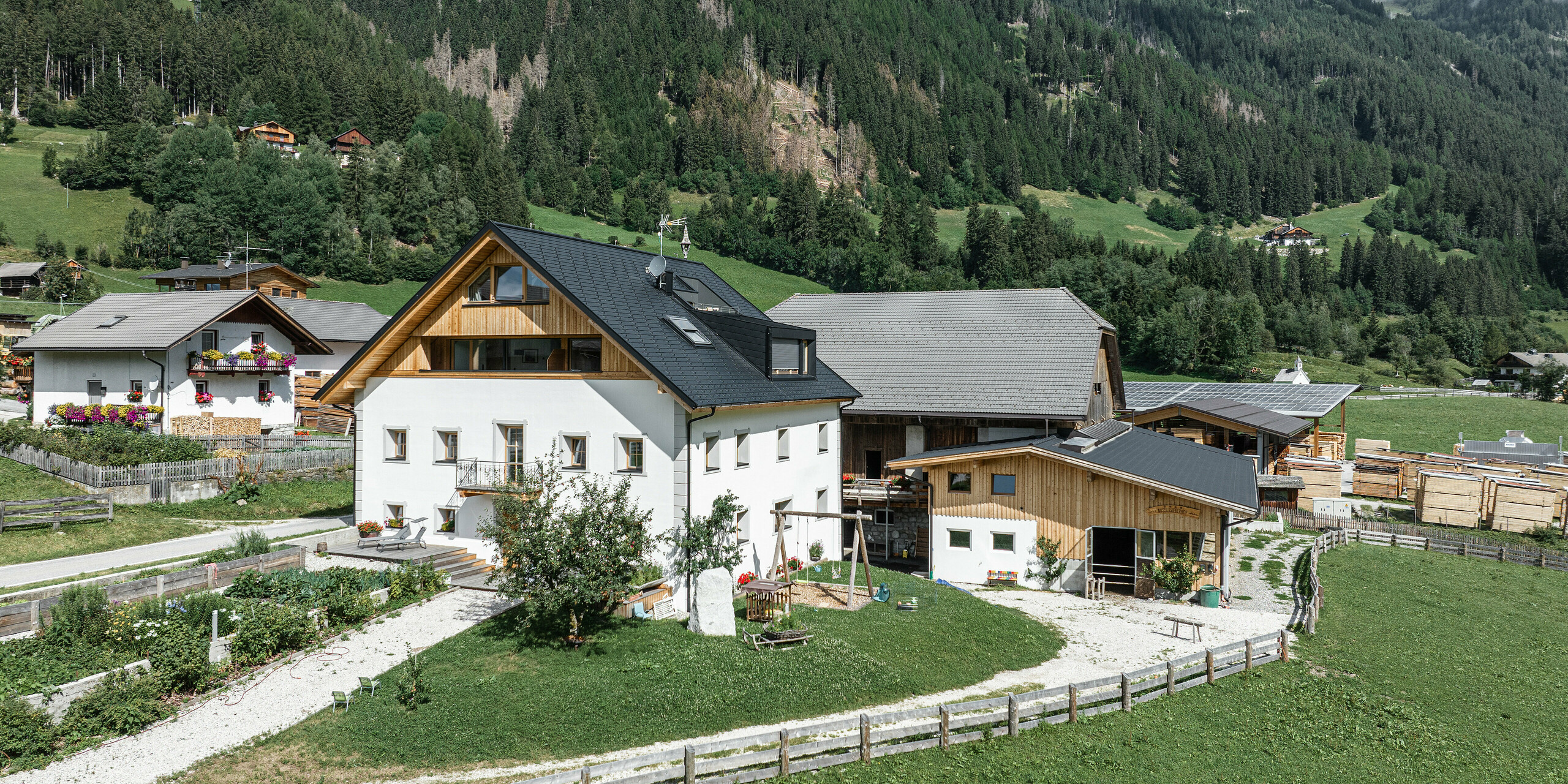 Pohled z ptačí perspektivy na Ausserwegerhof v Jižním Tyrolsku se střechou PREFA s dlouhou životností v barvě P.10 antracit. Prázdninové apartmány jsou zasazeny do zelené krajiny údolí Antholz s malebnými lesy a horami v pozadí. Robustní střešní šindel PREFA DS.19 nabízí ochranu tradičním budovám v teplých letních měsících i v ledových zimních podmínkách.